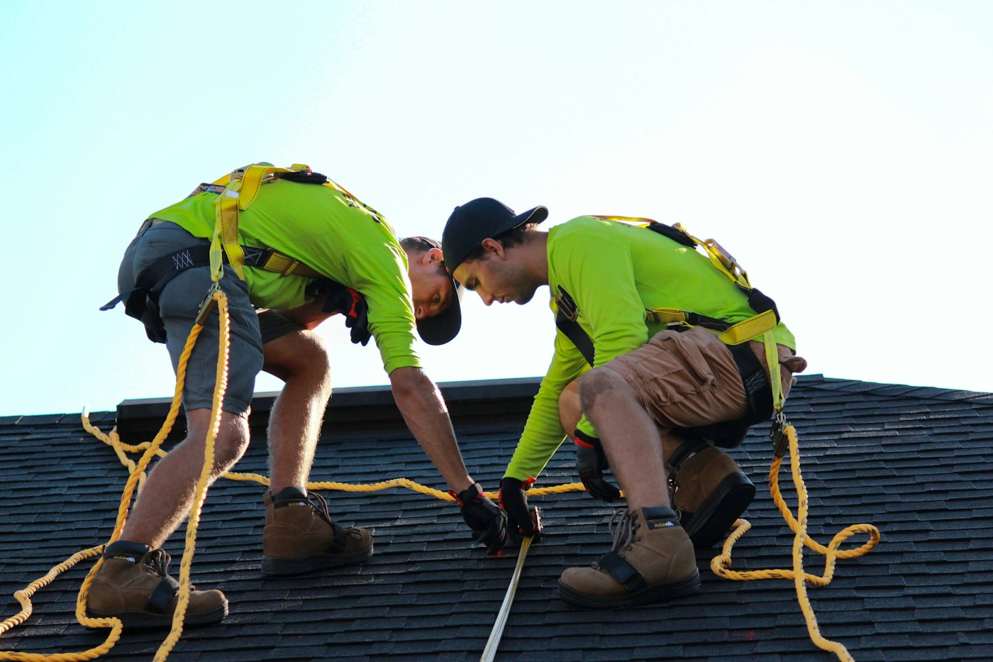 Two roofers measuring and laying shingles on a roof