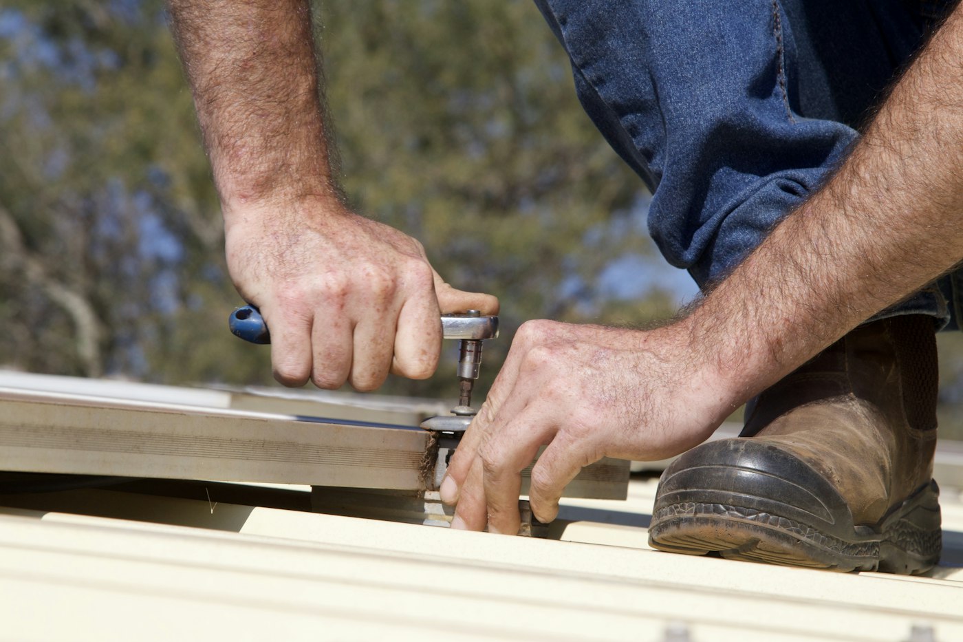 Roofer fastening a metal roof panel with a power tool