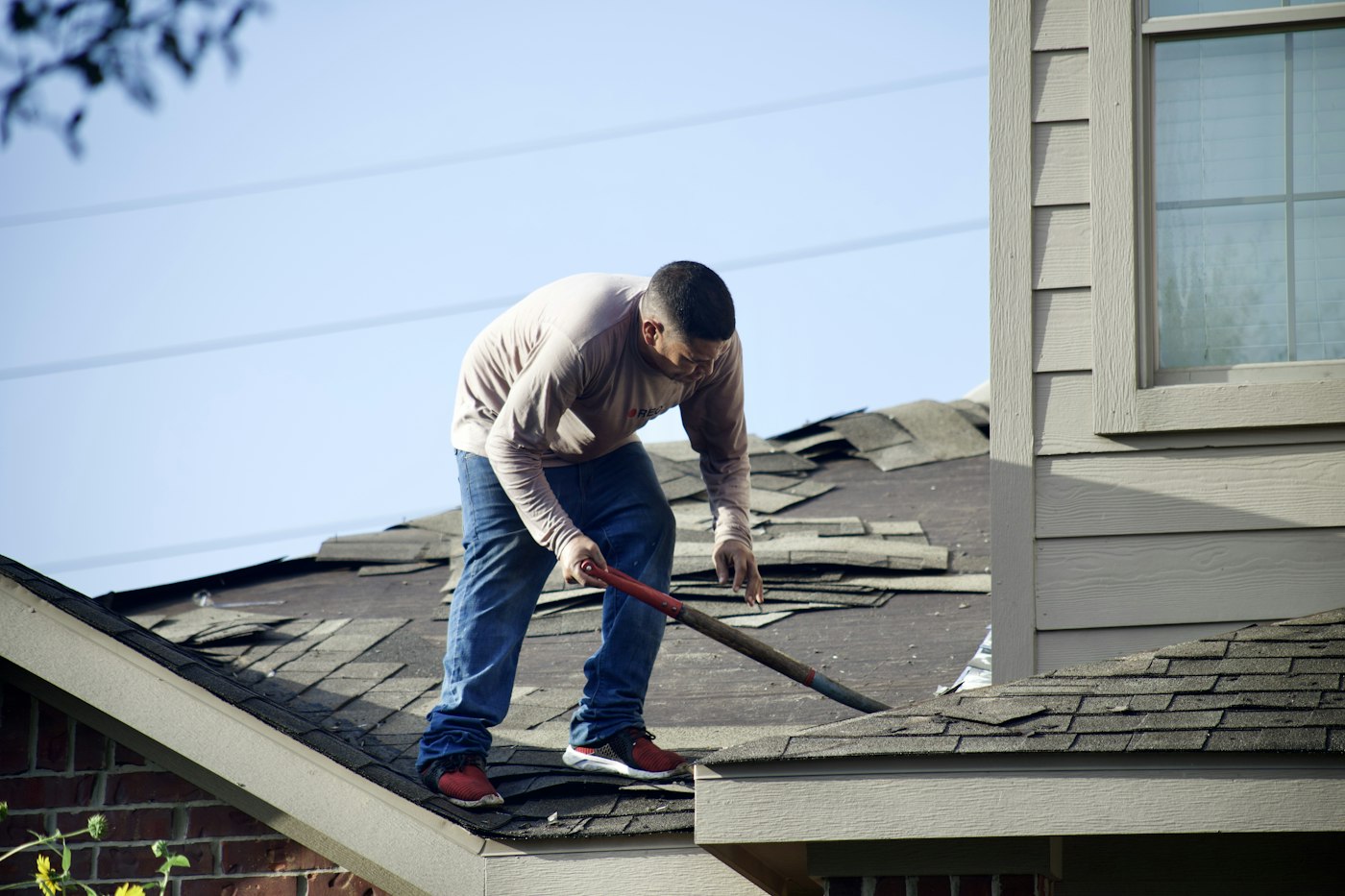 Roofer tearing off old asphalt shingles from a house